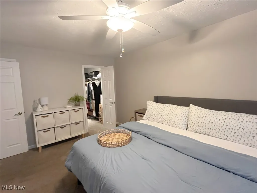 Bedroom featuring dark carpet, a ceiling fan, a walk in closet, and a textured ceiling
