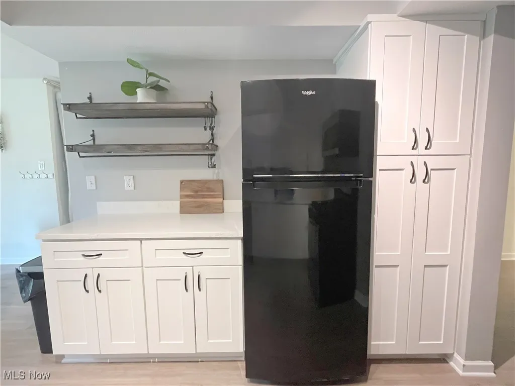 Kitchen featuring open shelves, white cabinets, freestanding refrigerator, and light wood finished floors