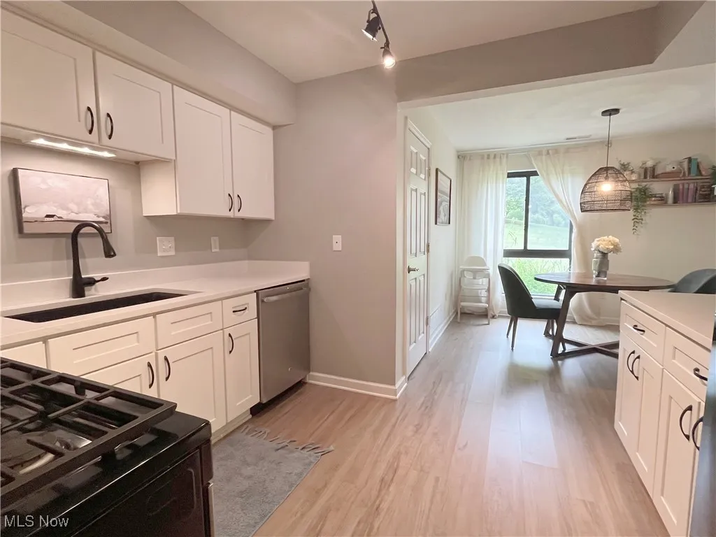 Kitchen featuring white cabinets, black range with gas cooktop, light wood finished floors, and stainless steel dishwasher