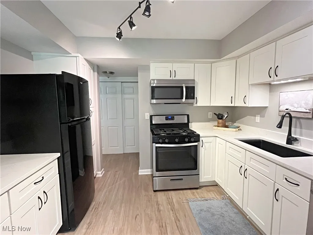 Kitchen with appliances with stainless steel finishes, white cabinets, light wood-style flooring, and light stone counters