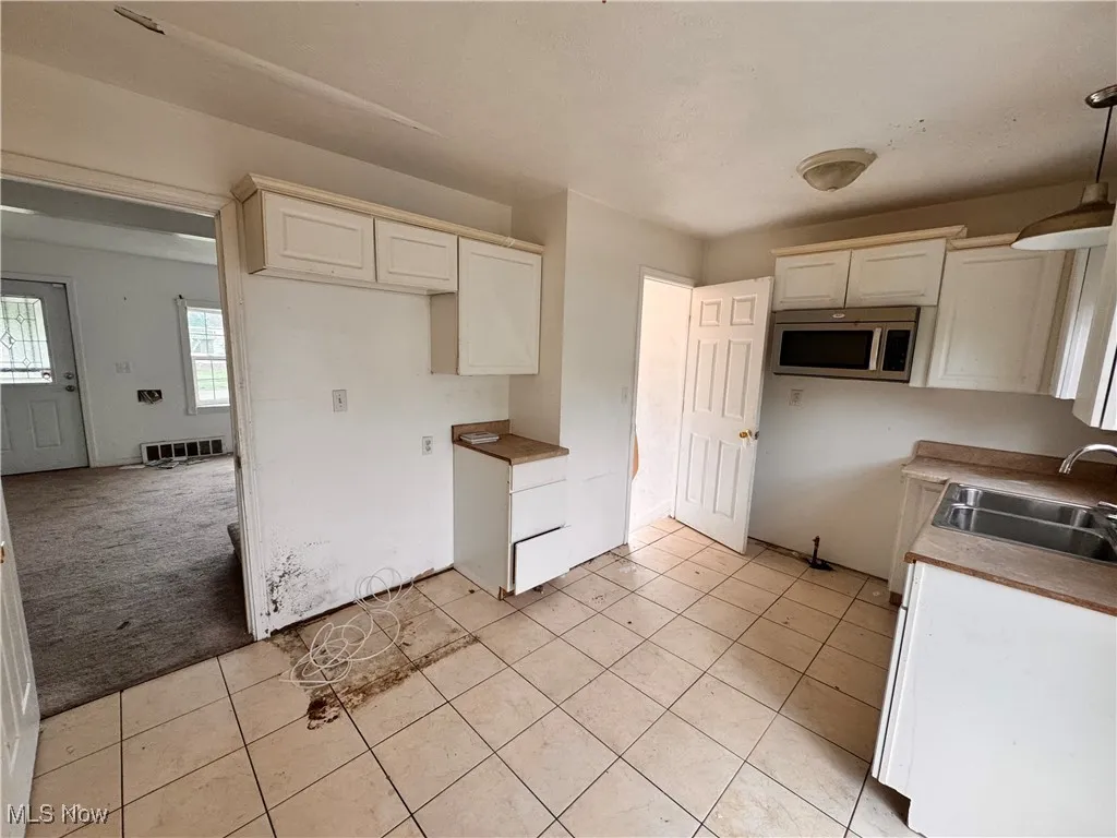 Kitchen with white cabinetry, light colored carpet, stainless steel microwave, light tile patterned flooring, and decorative light fixtures