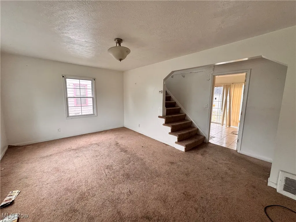 Unfurnished living room with a textured ceiling, carpet, and stairs