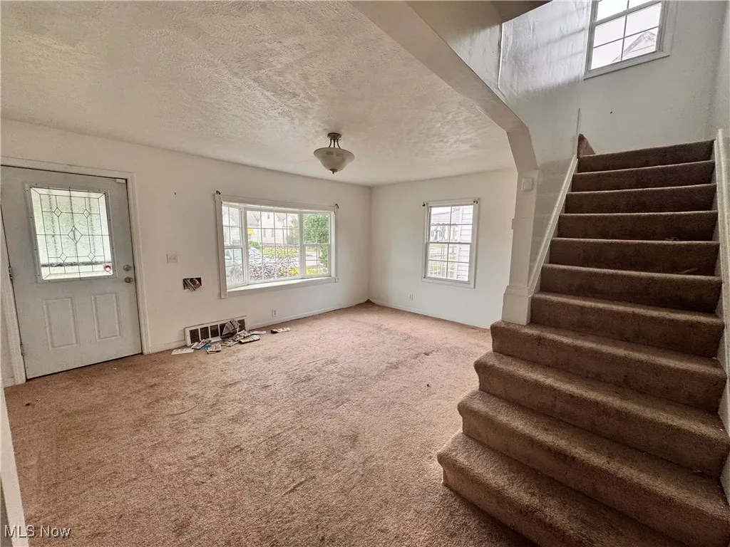 Unfurnished living room featuring healthy amount of natural light, carpet, a textured ceiling, and stairway