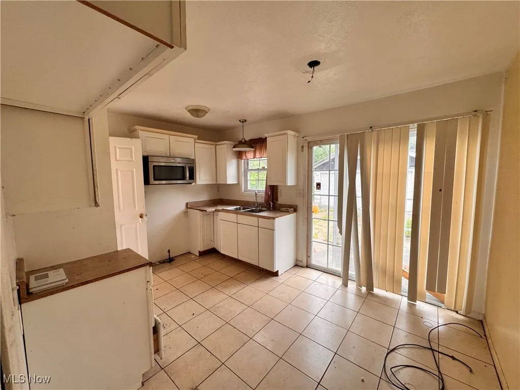 Kitchen featuring decorative light fixtures, stainless steel microwave, light tile patterned flooring, white cabinetry, and a textured ceiling