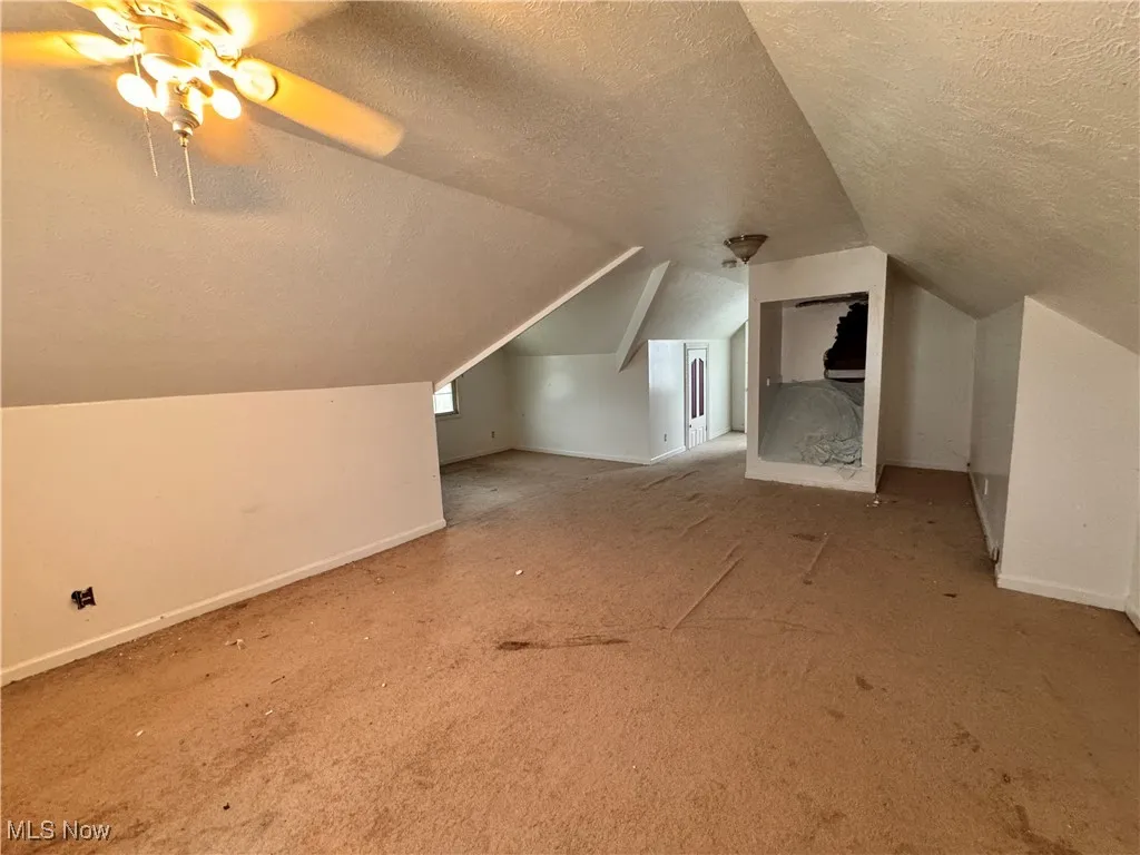 Bonus room with a textured ceiling, carpet flooring, vaulted ceiling, and ceiling fan