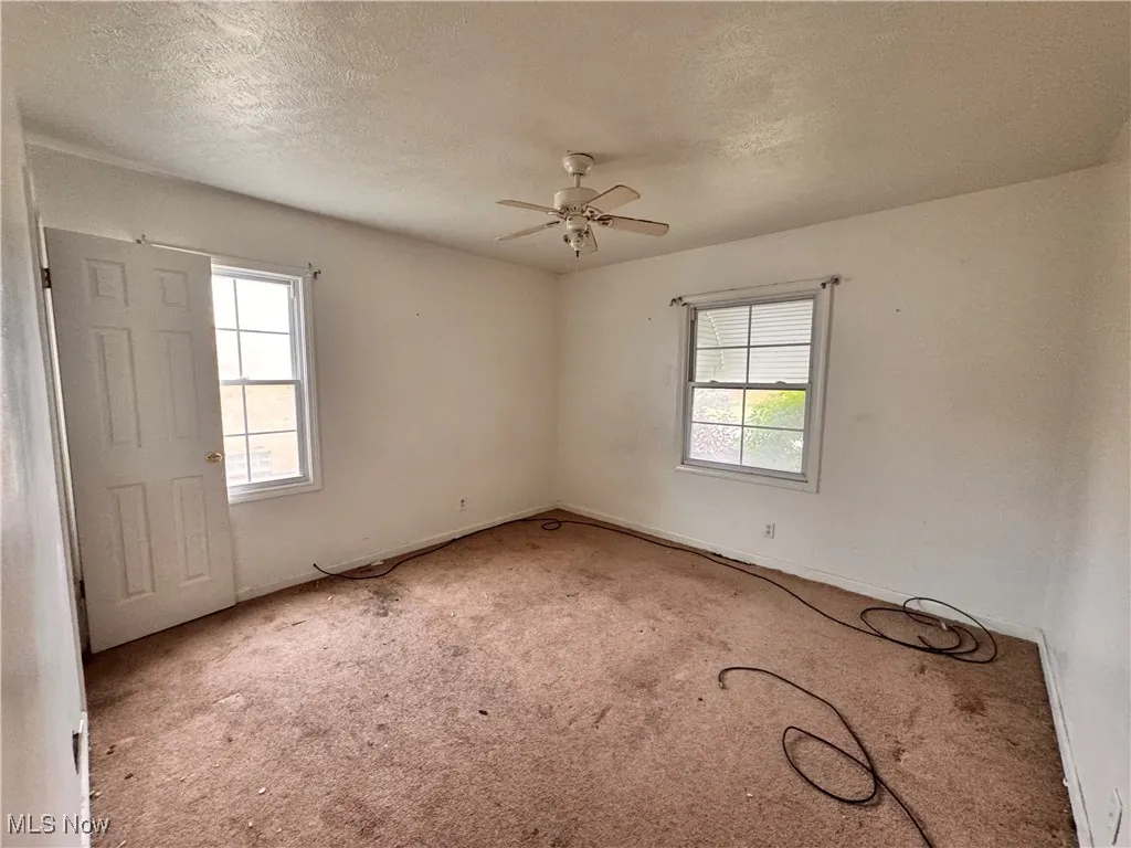 Carpeted empty room featuring a textured ceiling and ceiling fan