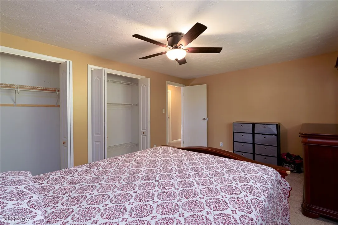 Primary bedroom featuring two closets, a textured ceiling, and a ceiling fan