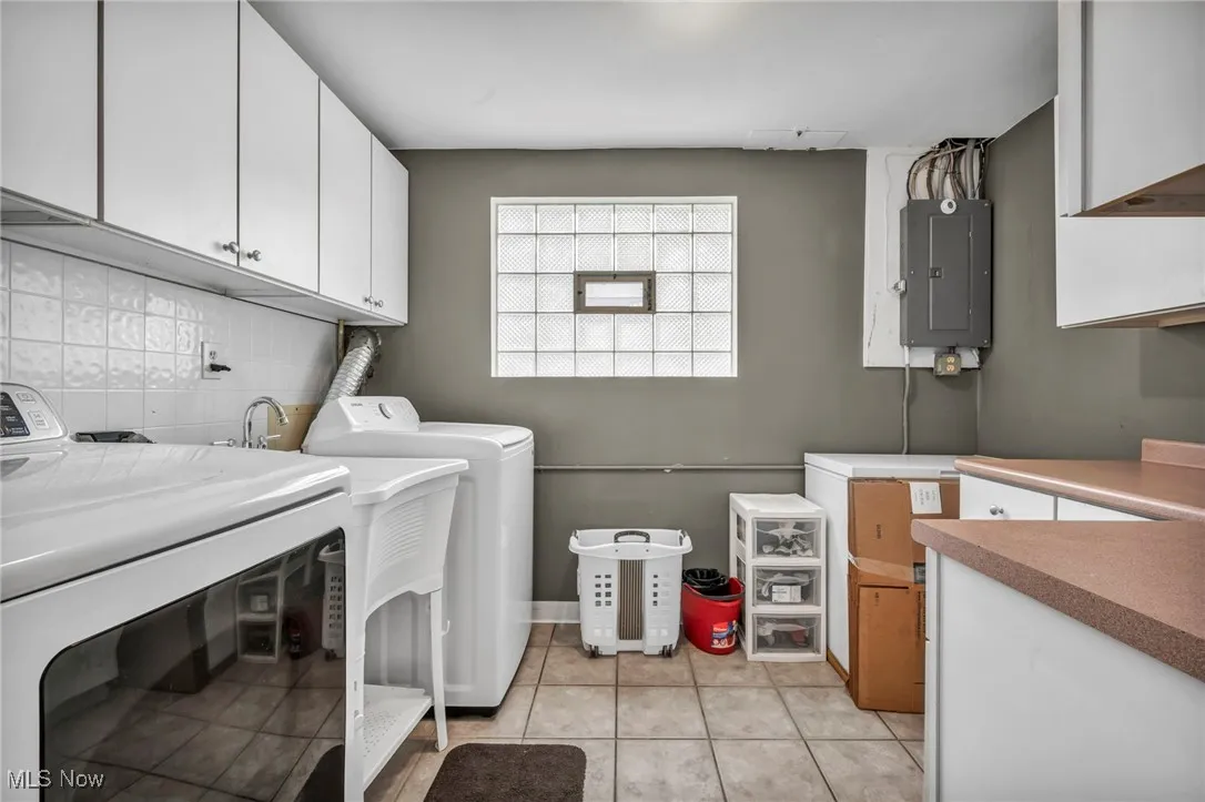 Laundry area featuring cabinet space, light tile patterned floors, electric panel, and washer and clothes dryer