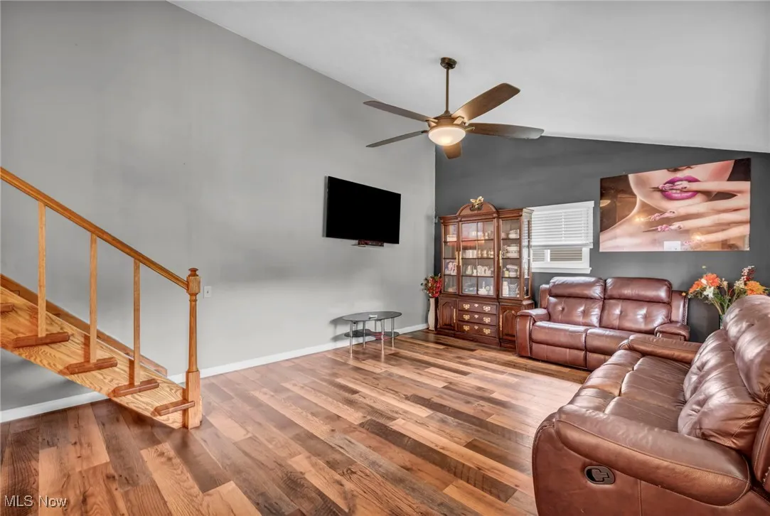 Living area featuring wood finished floors, ceiling fan, high vaulted ceiling, and stairway