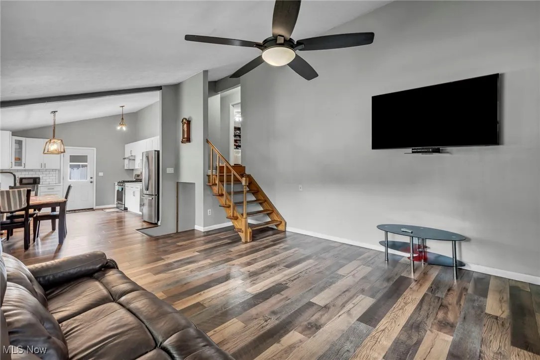 Living room with vaulted ceiling, dark wood finished floors, stairs, and a ceiling fan