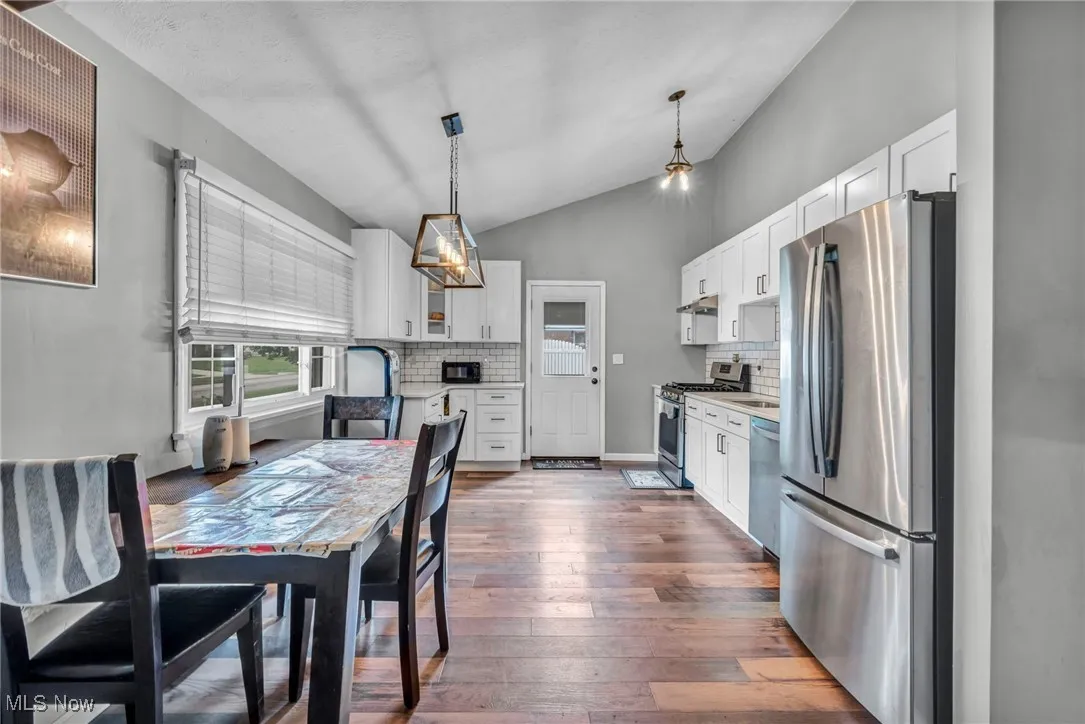 Kitchen featuring stainless steel appliances, tasteful backsplash, vaulted ceiling, white cabinetry, and hanging light fixtures
