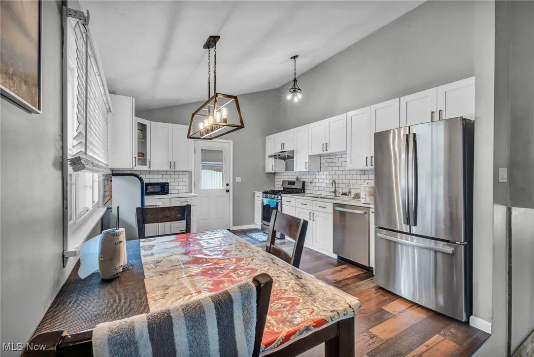 Kitchen featuring stainless steel appliances, vaulted ceiling, white cabinetry, dark wood-style floors, and decorative backsplash