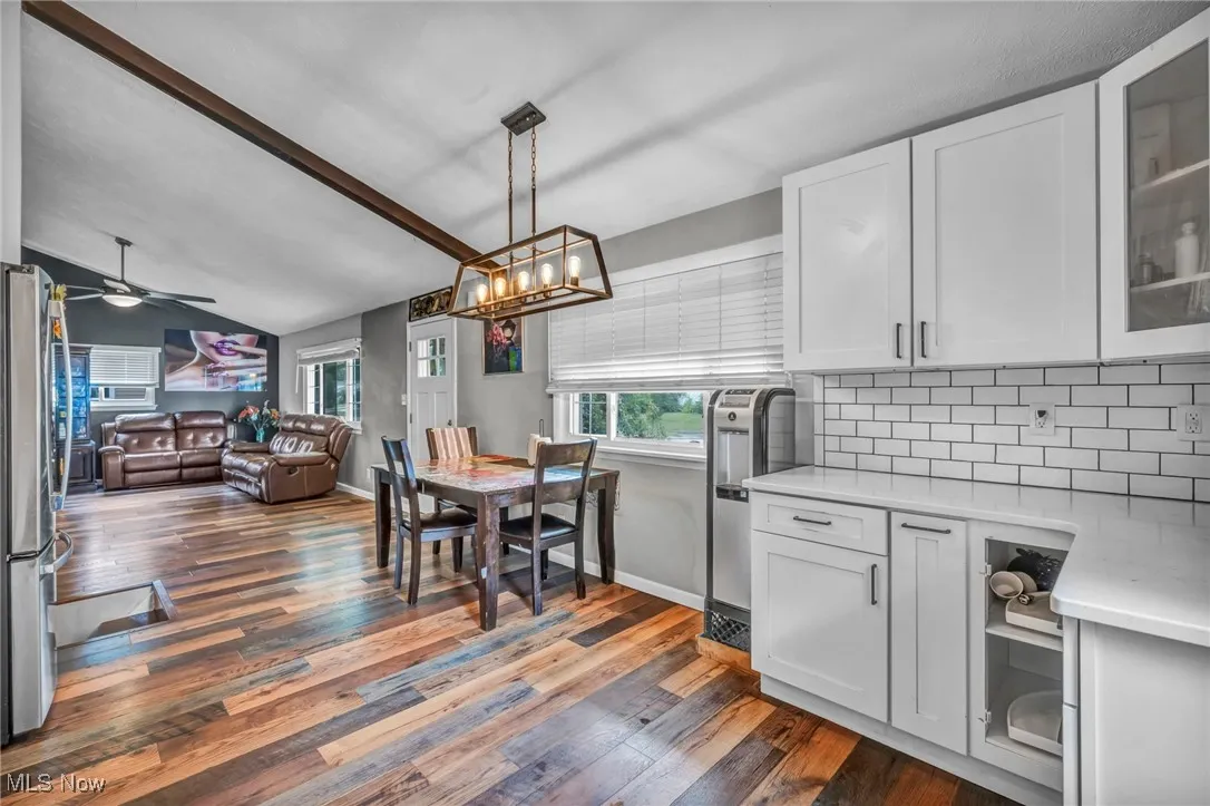Kitchen with white cabinetry, light stone counters, vaulted ceiling, dark wood-style flooring, and freestanding refrigerator