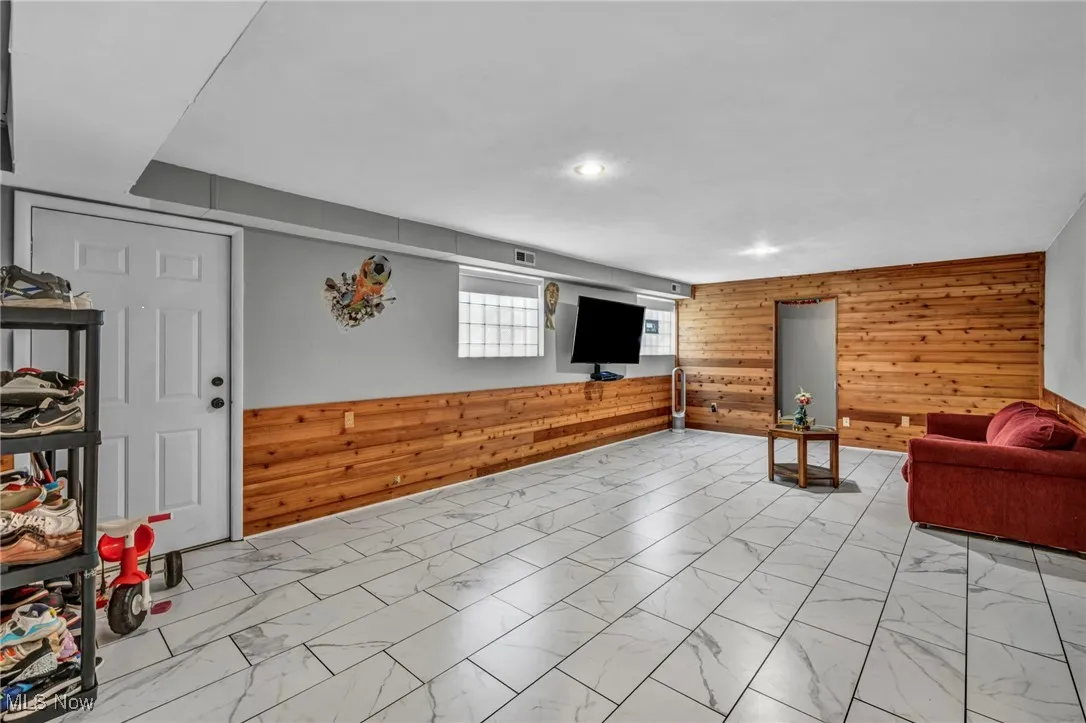 Living area featuring wood walls, light marble finish flooring, and recessed lighting