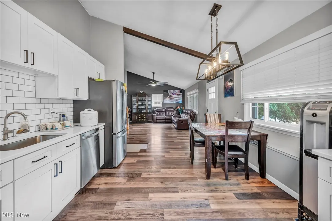 Kitchen featuring lofted ceiling, white cabinetry, hanging light fixtures, tasteful backsplash, and light wood finished floors