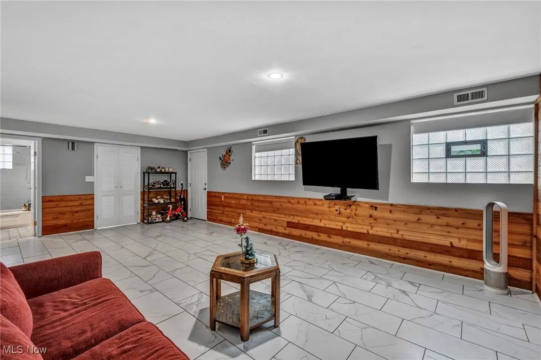 Living room with wooden walls, wainscoting, healthy amount of natural light, light marble finish flooring, and recessed lighting