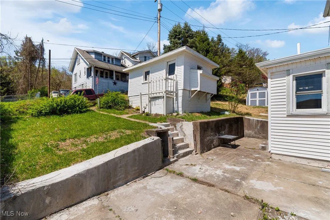 View of side of property featuring a lawn, a storage shed, and stairs