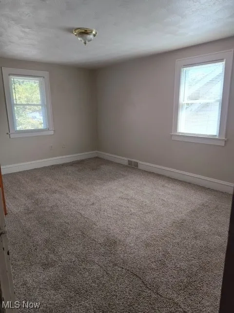 Empty room with light colored carpet and baseboards