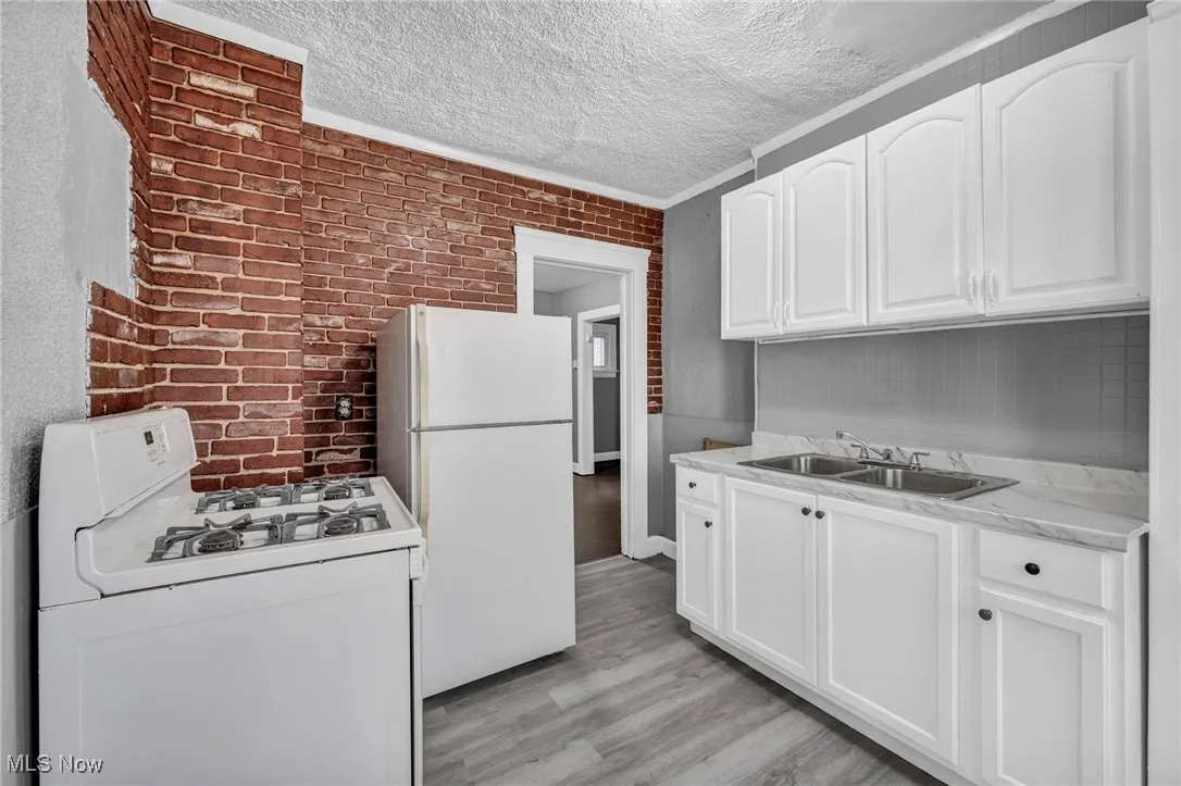 Kitchen featuring white appliances, white cabinets, light countertops, brick wall, and light wood finished floors