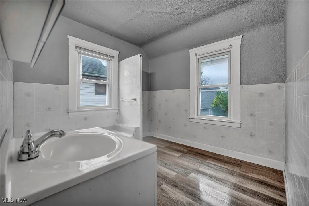 Bathroom with a wainscoted wall, wood finished floors, vanity, a textured ceiling, and tile walls