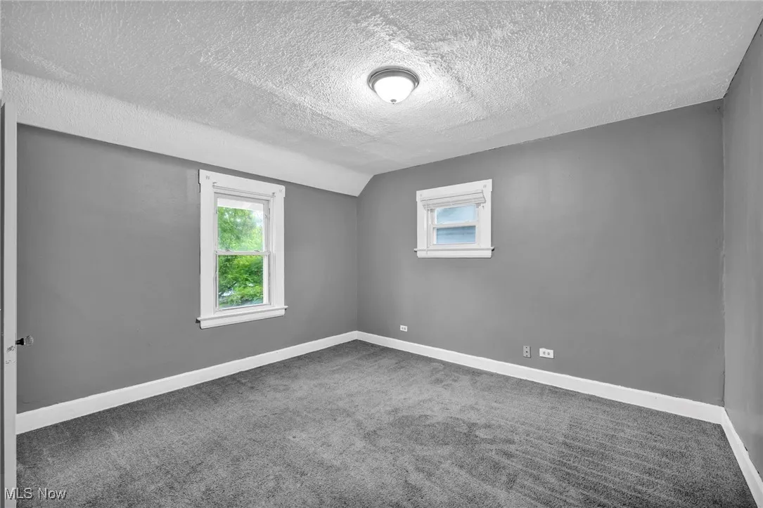 Carpeted empty room with lofted ceiling and a textured ceiling