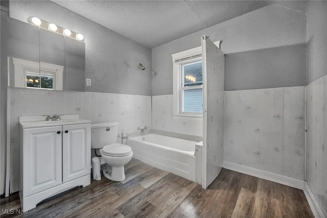 Bathroom featuring a textured wall, a bath, dark wood-style floors, vanity, and tile walls
