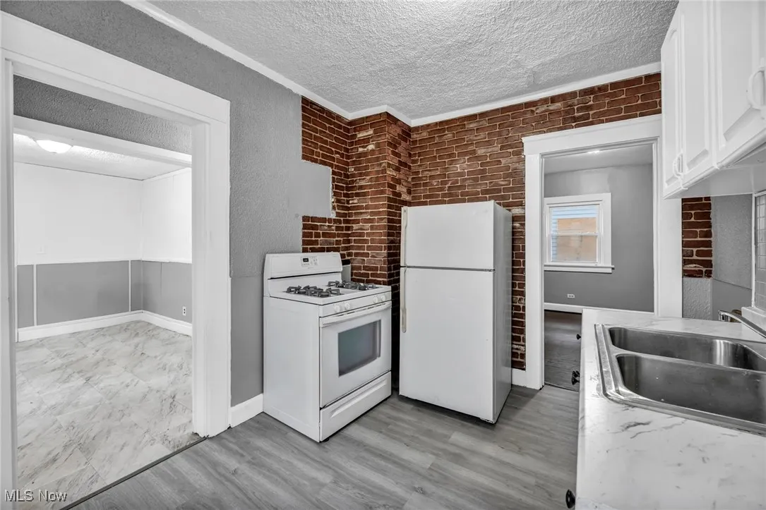 Kitchen featuring white appliances, white cabinets, brick wall, a textured ceiling, and light countertops