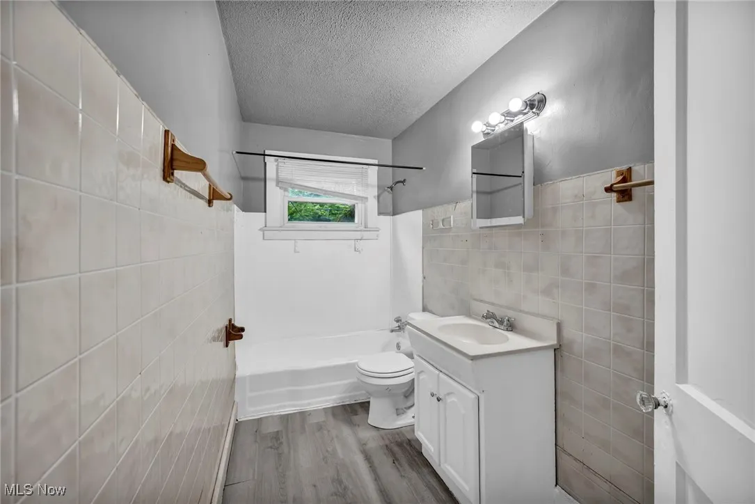 Bathroom featuring tile walls, shower / washtub combination, a textured ceiling, vanity, and light wood-style flooring