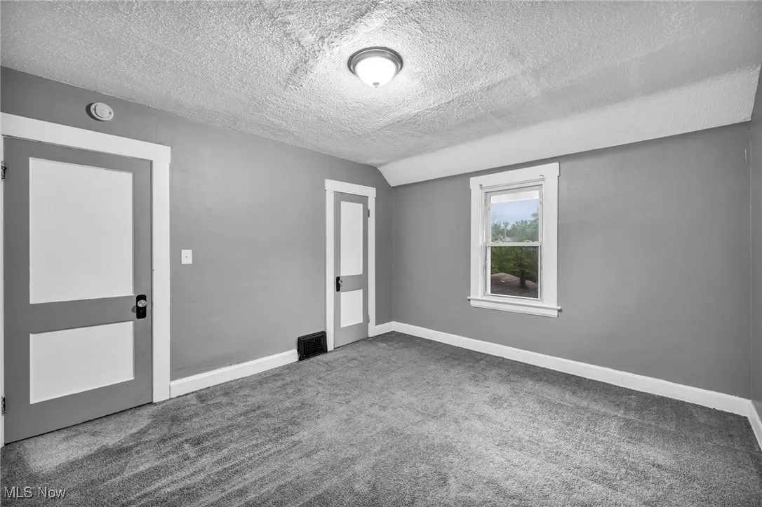 Carpeted spare room featuring a textured ceiling and lofted ceiling