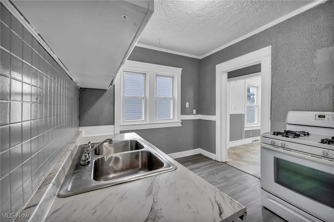 Kitchen featuring white gas stove, light wood-style flooring, a textured ceiling, light countertops, and crown molding