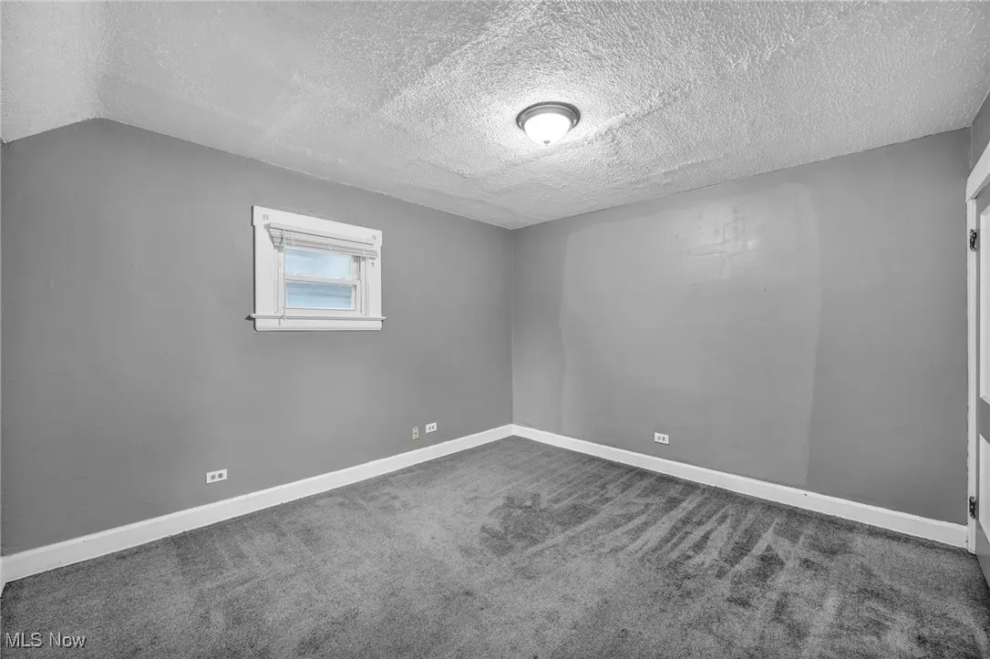 Carpeted spare room with a textured ceiling and baseboards