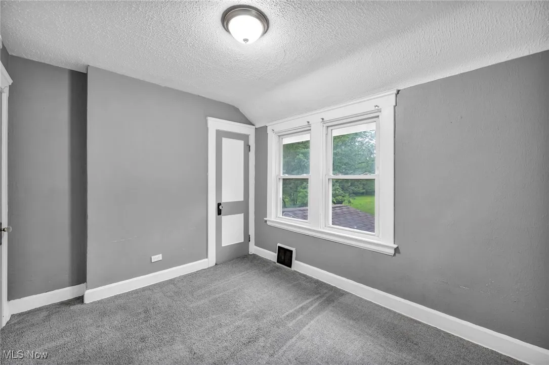 Carpeted empty room with vaulted ceiling and a textured ceiling