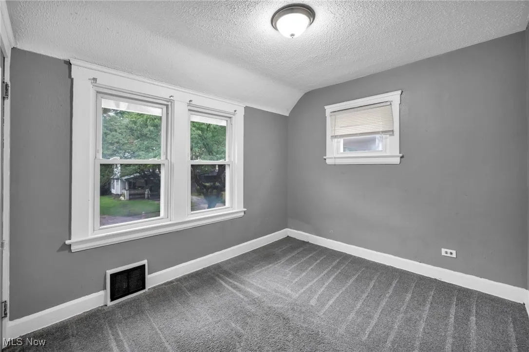 Carpeted spare room with a textured ceiling and vaulted ceiling
