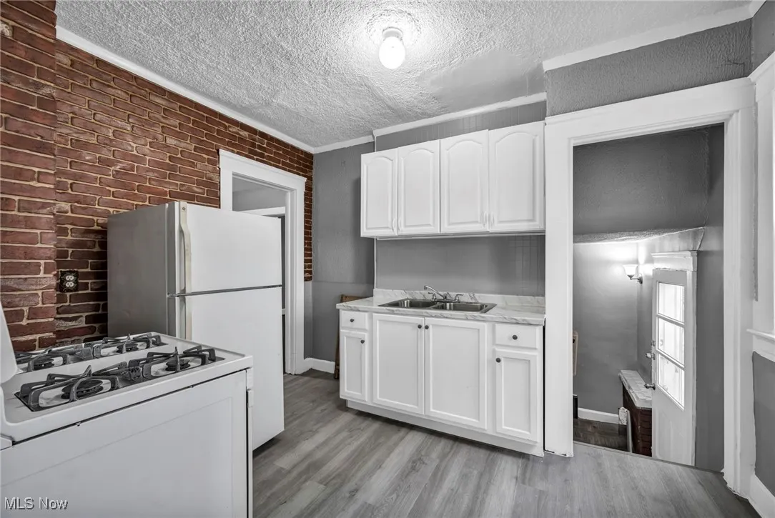 Kitchen featuring brick wall, light countertops, white appliances, white cabinets, and light wood-type flooring