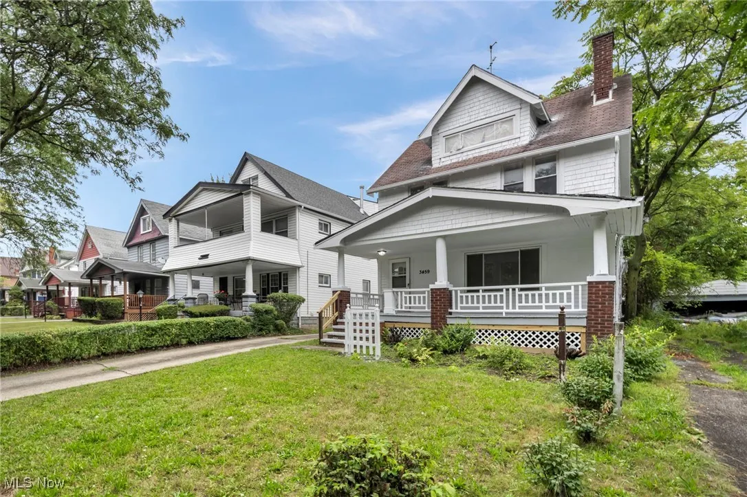 American foursquare style home featuring a porch, a chimney, a front yard, and roof with shingles