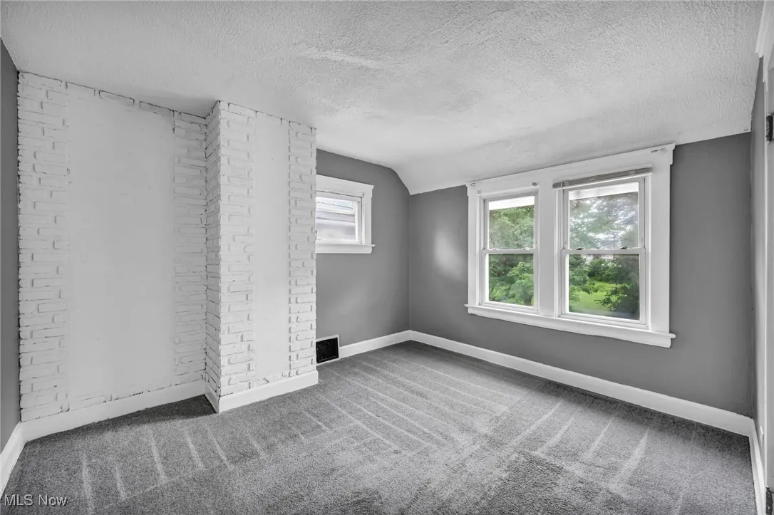 Unfurnished room with carpet flooring, a textured ceiling, and vaulted ceiling