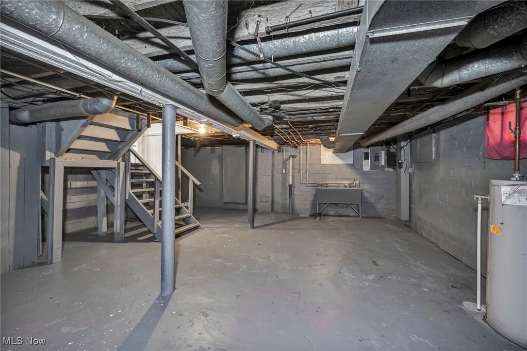 Unfinished below grade area featuring stairway, gas water heater, and electric panel