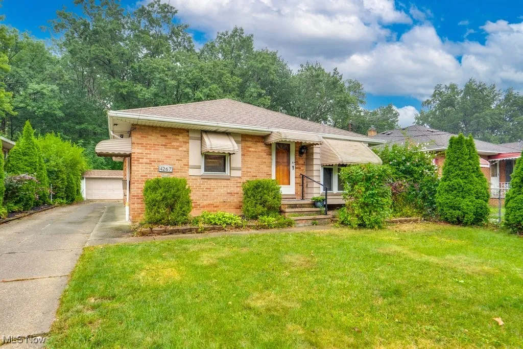 View of front of home featuring brick siding, an outdoor structure, a front lawn, roof with shingles, and a detached garage