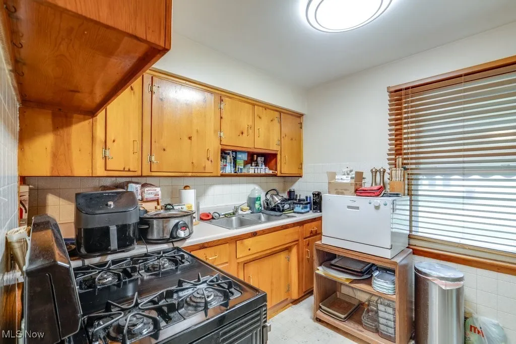 Kitchen with decorative backsplash, light countertops, black gas range oven, open shelves, and brown cabinets