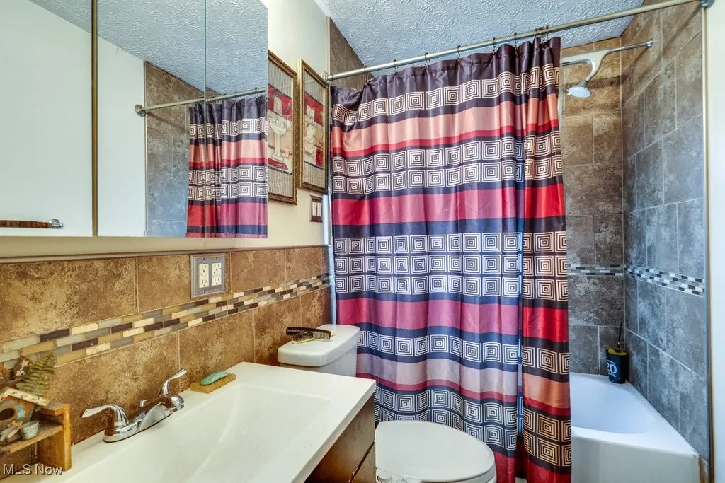 Full bathroom with shower / tub combo with curtain, a textured ceiling, vanity, and tile walls