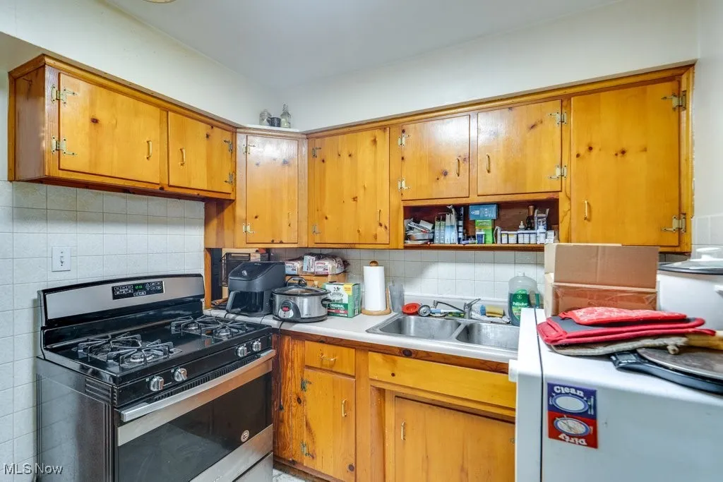 Kitchen with stainless steel range with gas stovetop, decorative backsplash, light countertops, and brown cabinetry