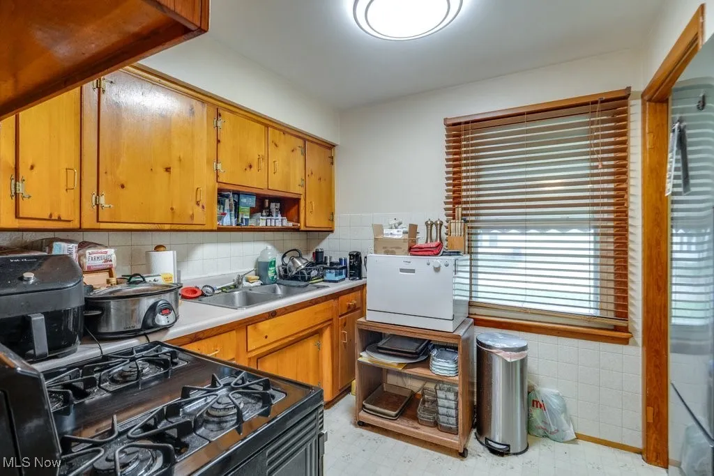 Kitchen featuring light countertops, brown cabinets, tasteful backsplash, gas stove, and light floors