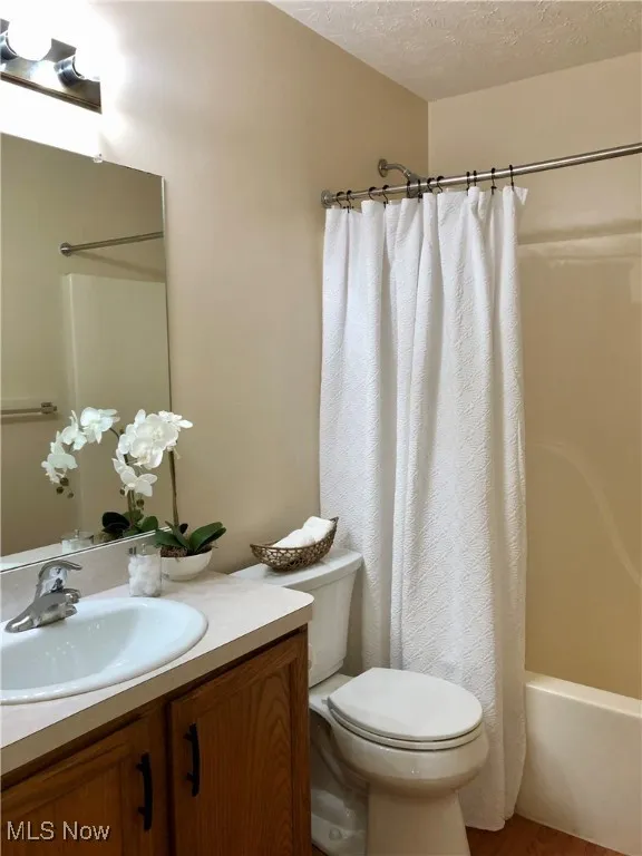 Full bathroom with a textured ceiling, shower / bathtub combination with curtain, vanity, and wood finished floors