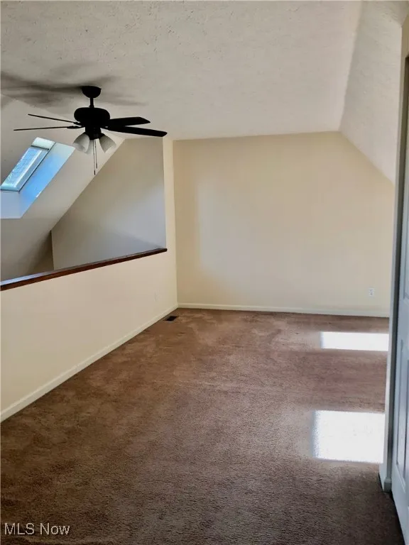 Spare room featuring vaulted ceiling, a skylight, a textured ceiling, carpet, and ceiling fan