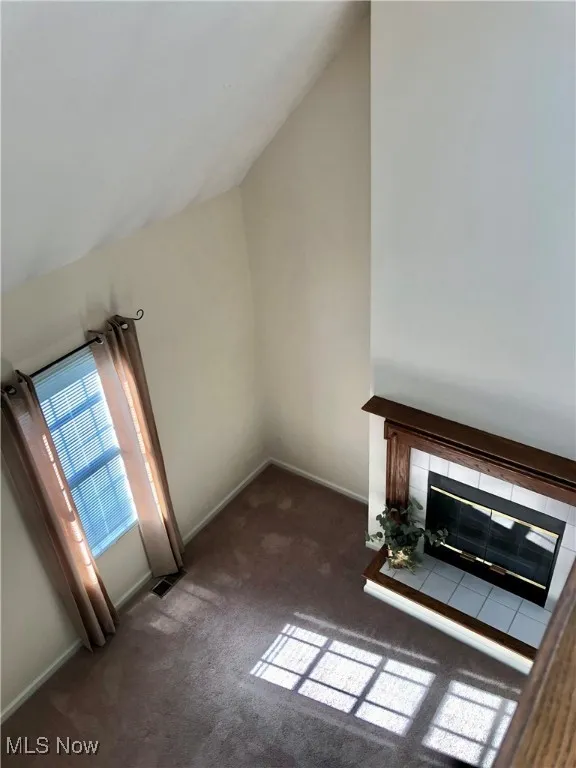 Unfurnished living room featuring vaulted ceiling, carpet flooring, and a tile fireplace