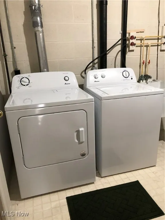 Laundry room featuring light flooring, washing machine and dryer, and concrete block wall