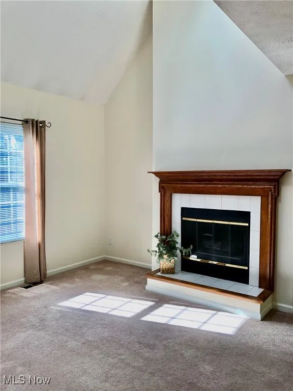 Unfurnished living room featuring a fireplace, carpet floors, high vaulted ceiling, and a textured ceiling