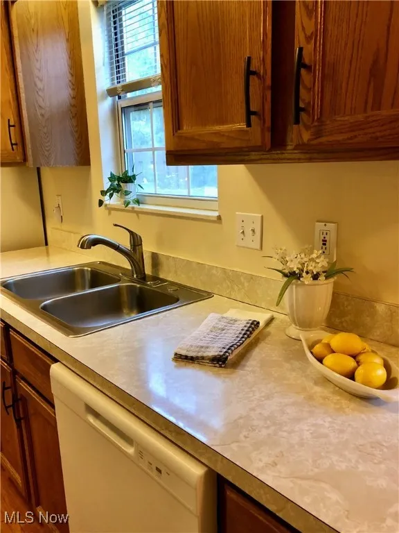 Kitchen featuring brown cabinetry, white dishwasher, and light countertops