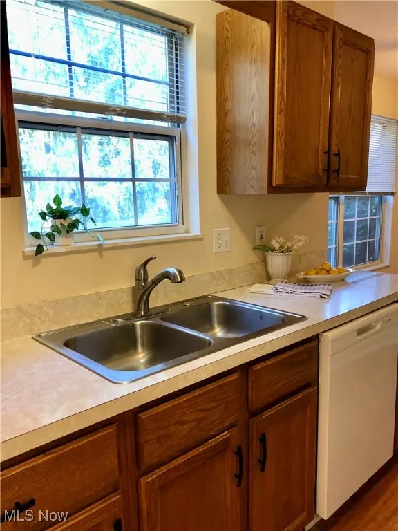 Kitchen featuring light countertops, white dishwasher, plenty of natural light, and brown cabinets
