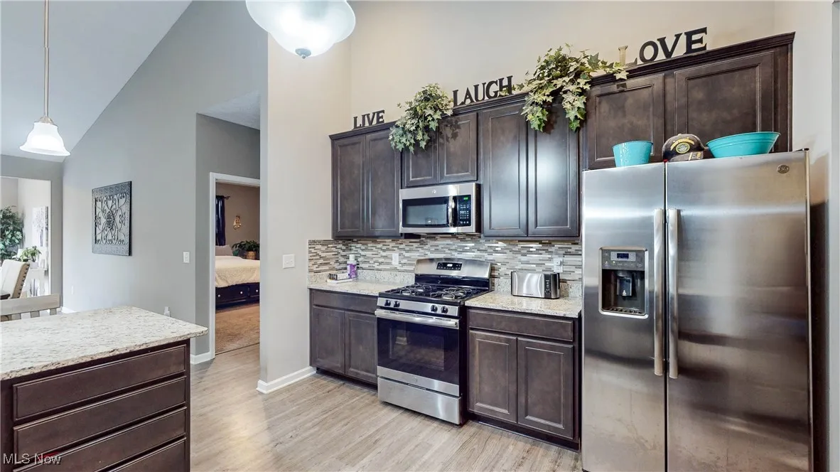 Kitchen with appliances with stainless steel finishes, dark brown cabinetry, tasteful backsplash, hanging light fixtures, and light wood finished floors